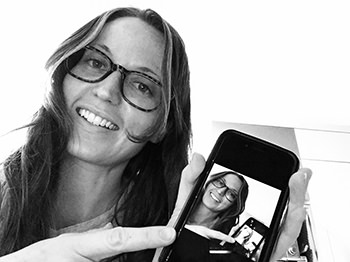 A photo of the author Greta C Wink, smiling, with a phone